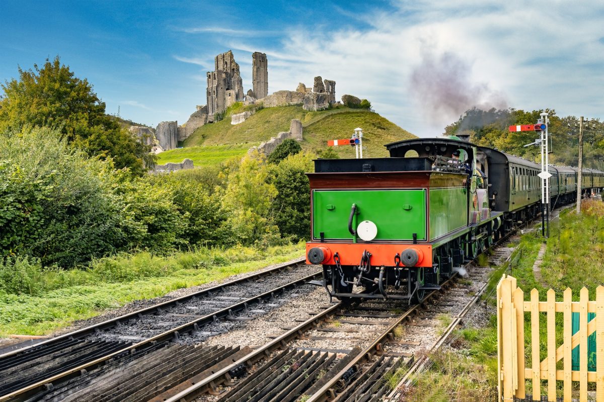 Steam train at Corfe Castle station with Corfe Castle rising above the village in Dorset.