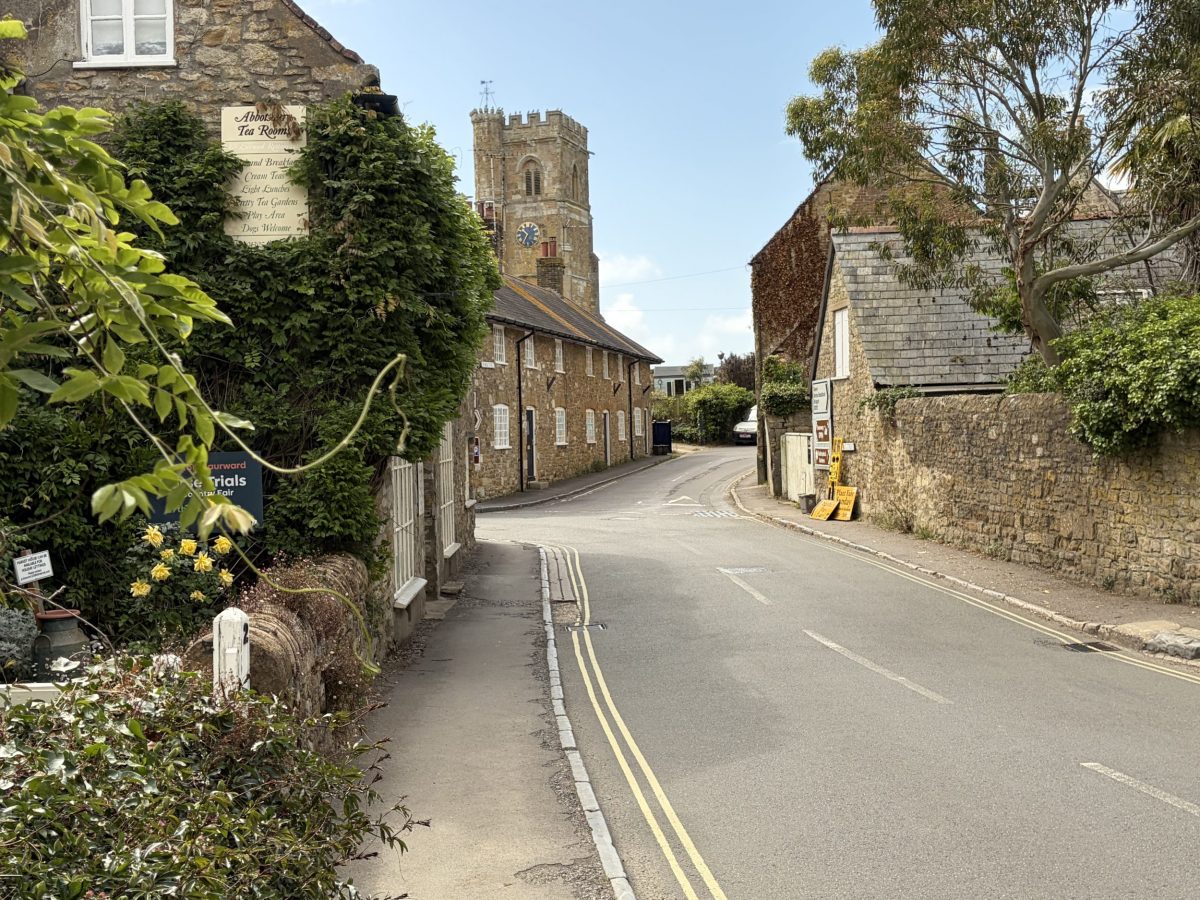 Historic street in Abbotsbury with traditional Dorset stone cottages and St Nicholas Church in the distance