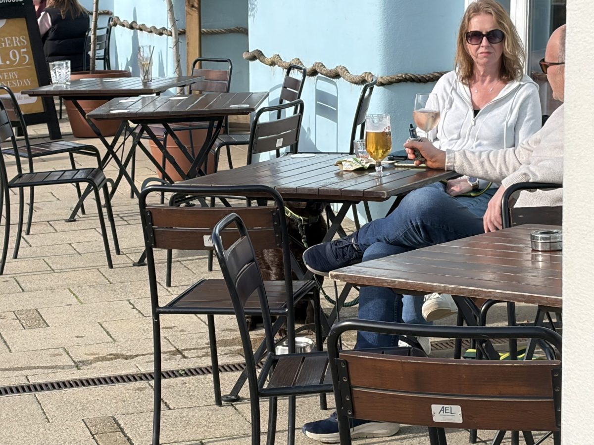 Couple enjoying drinks at an outdoor restaurant overlooking Weymouth Harbour on a sunny day.