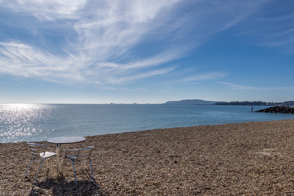 Outdoor seating overlooking Overcombe Beach with calm sea on a sunny day in Weymouth, Dorset.