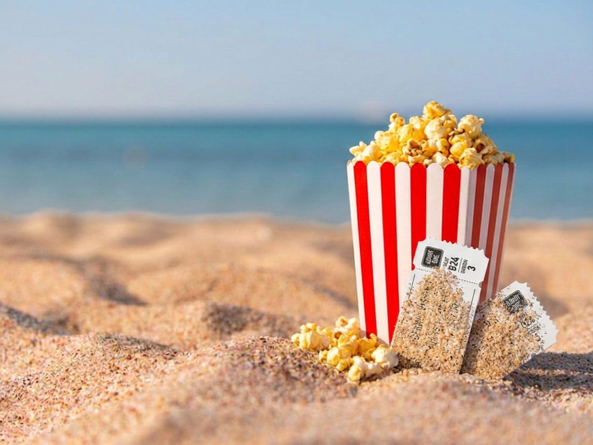 Bucket of popcorn on a sandy beach overlooking the sea, representing film tourism on Britain's coastline.