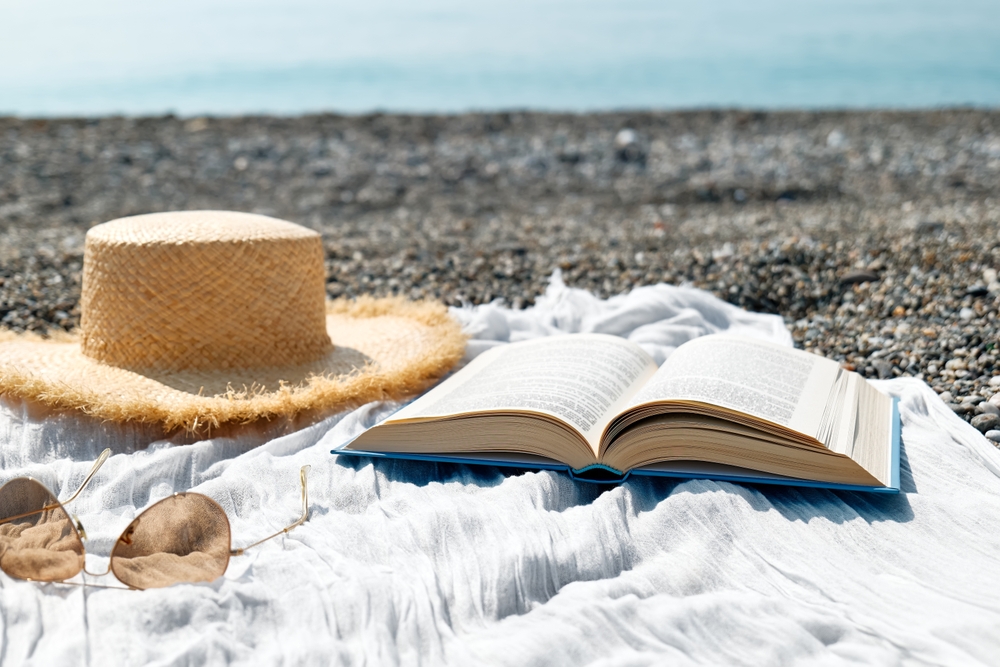 Open book, straw hat and sunglasses on a pebble beach overlooking the sea in Dorset.