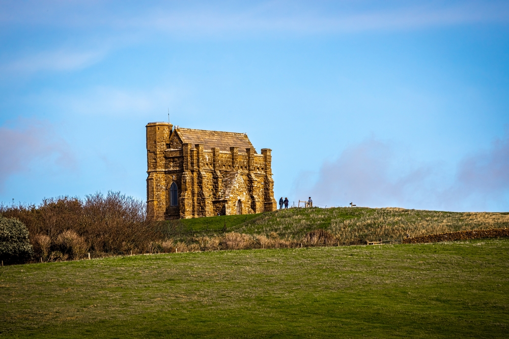 St Catherine's Chapel overlooking Abbotsbury, with green fields beneath a blue Dorset sky.