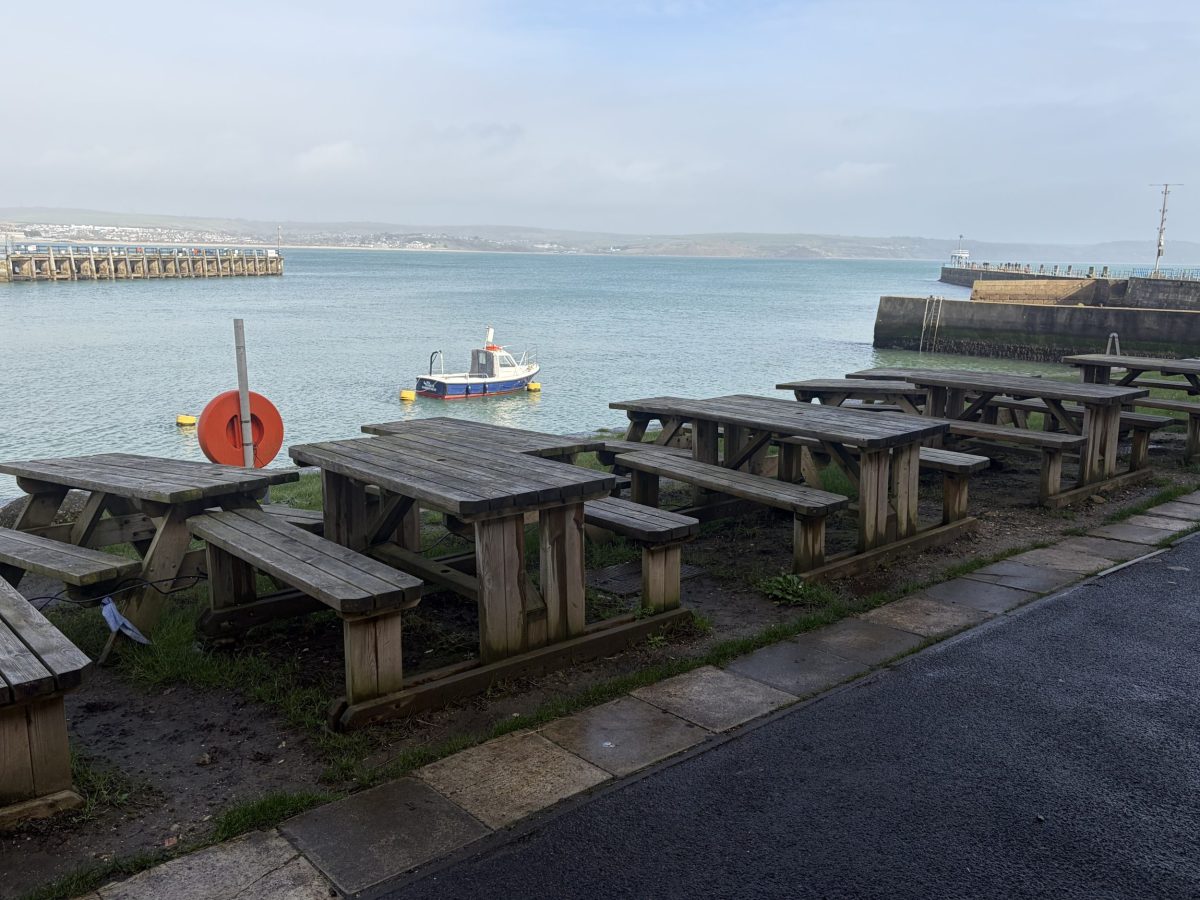 View from Stone Pier Café overlooking Weymouth Harbour as a boat leaves the harbour with the Dorset coastline beyond.