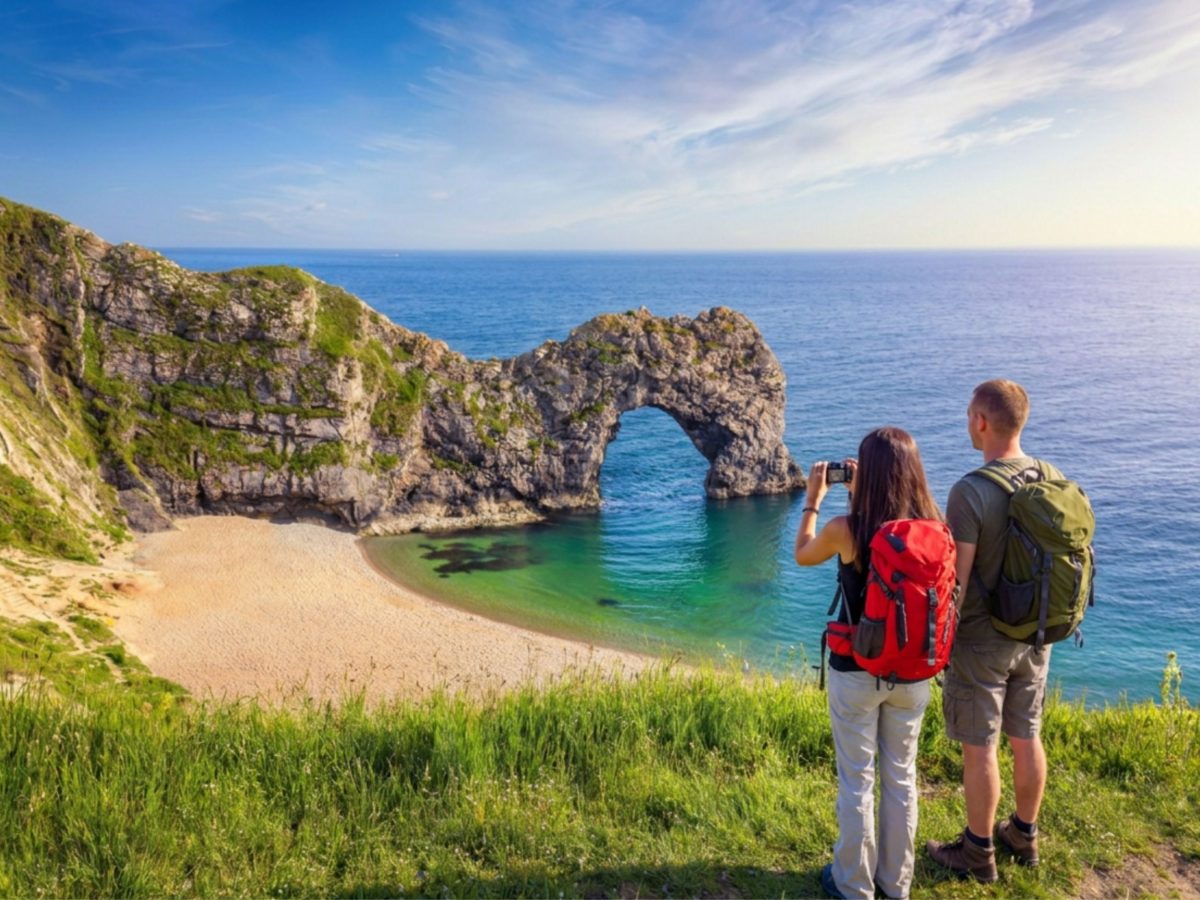 Two visitors photographing Durdle Door from the clifftop on Dorset's Jurassic Coast.