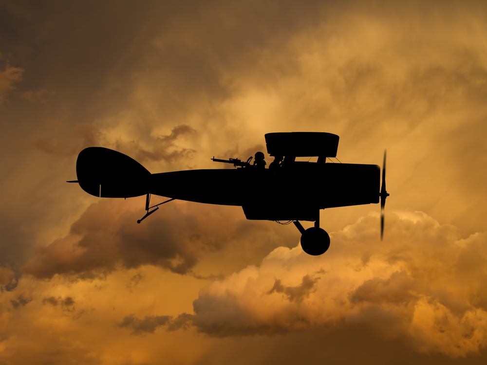 Silhouette of a vintage aircraft against an orange sunset sky