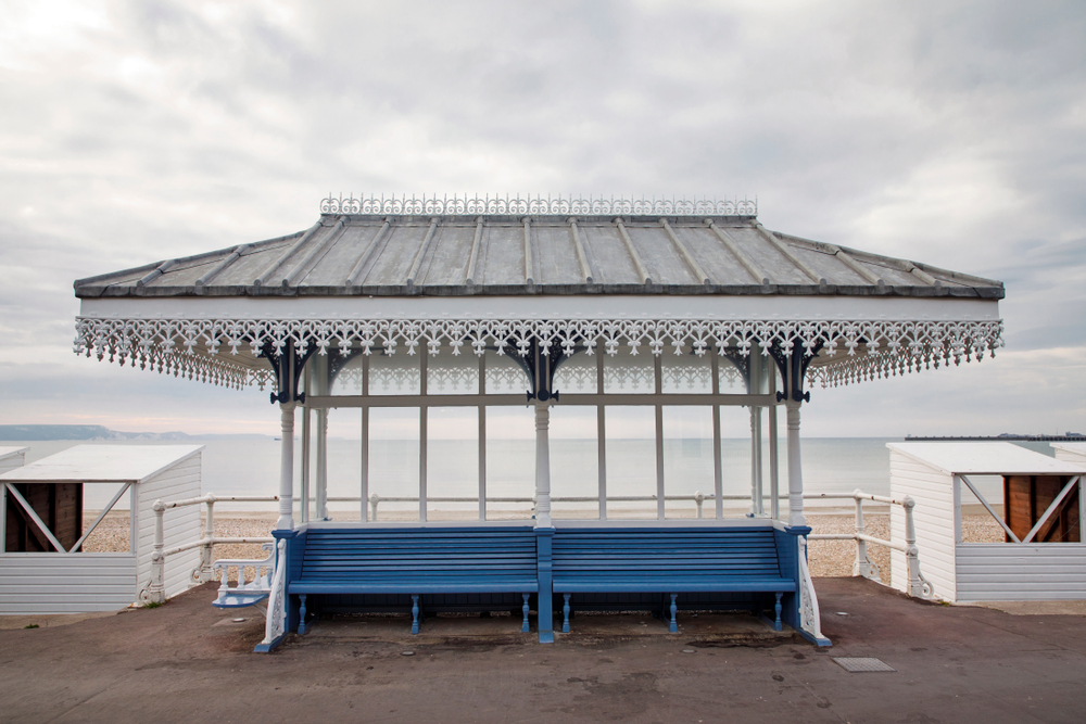 Victorian beach shelter on Weymouth Beach with calm sea and traditional beach huts in Dorset.