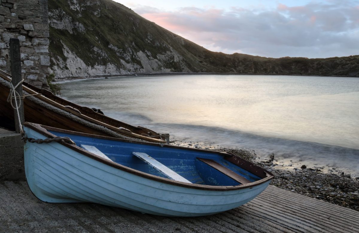 Small fishing boat resting ashore overlooking the clear waters of Lulworth Cove on Dorset's Jurassic Coast.