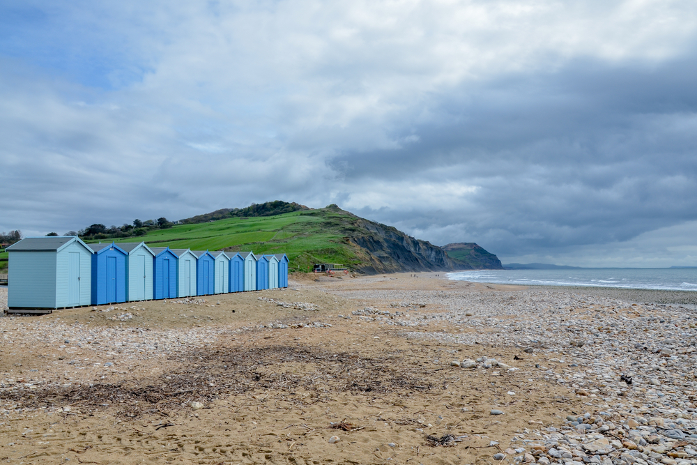 Beach huts on Charmouth Beach beneath the green cliffs of the Jurassic Coast in Dorset
