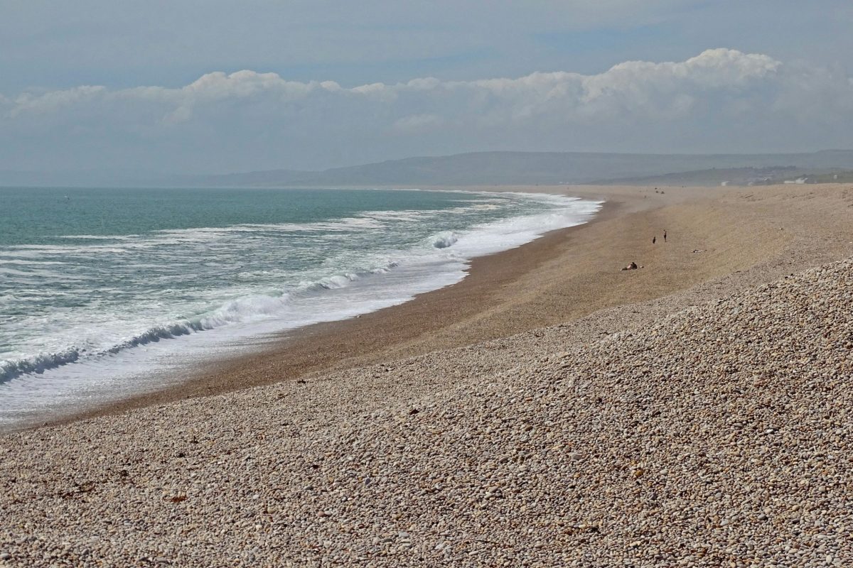 Long sweeping view of waves rolling onto Chesil Beach at Portland, Dorset.