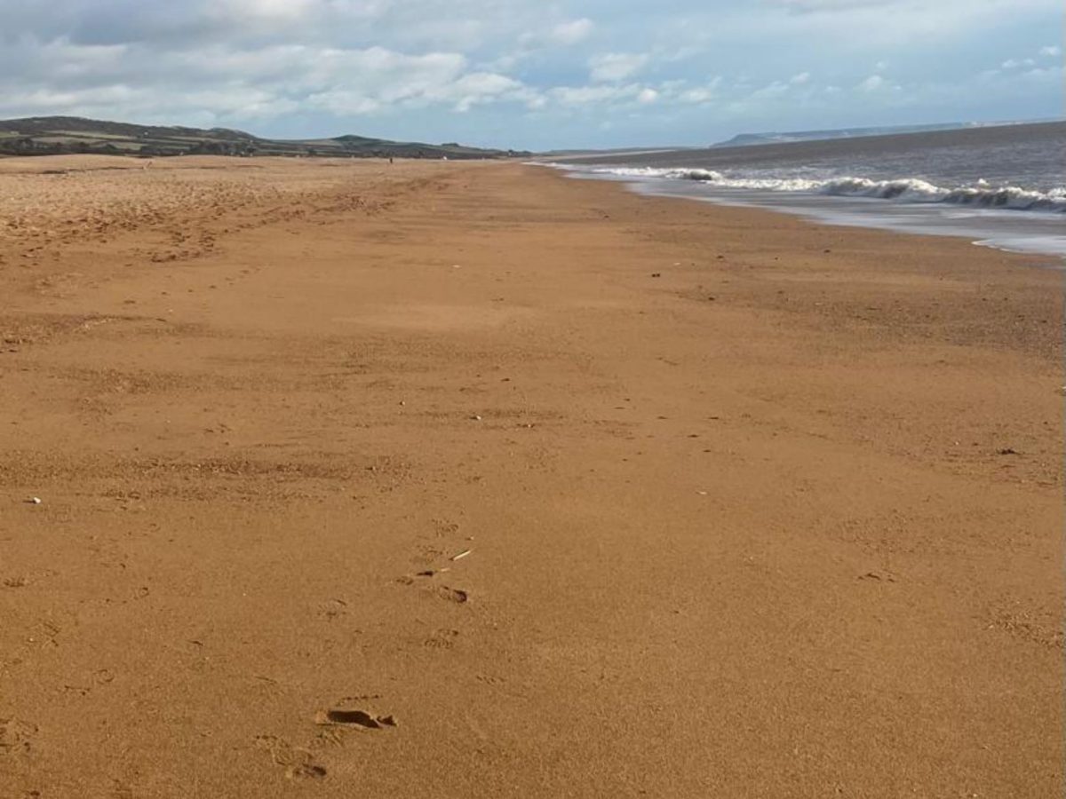 Empty sandy Cogden Beach, Dorset, with views towards Portland, underneath stormy skies