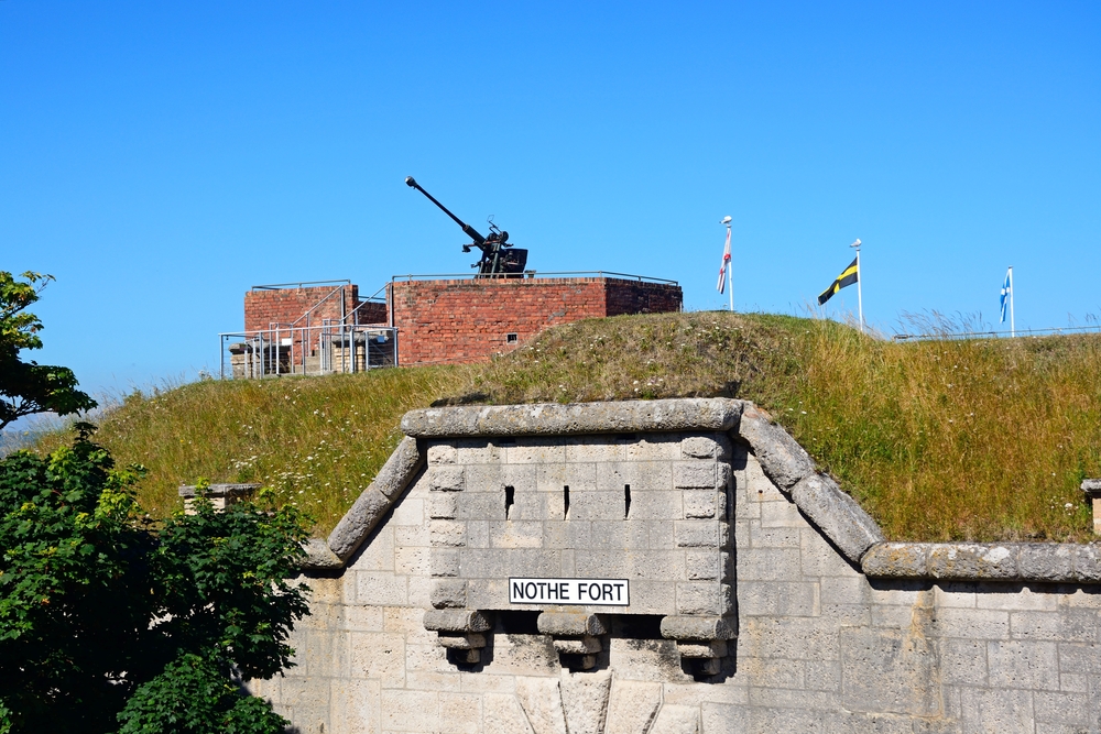 The entrance to Nothe Fort, Weymouth, Dorset, with World War Two military guns against a clear blue sky.
