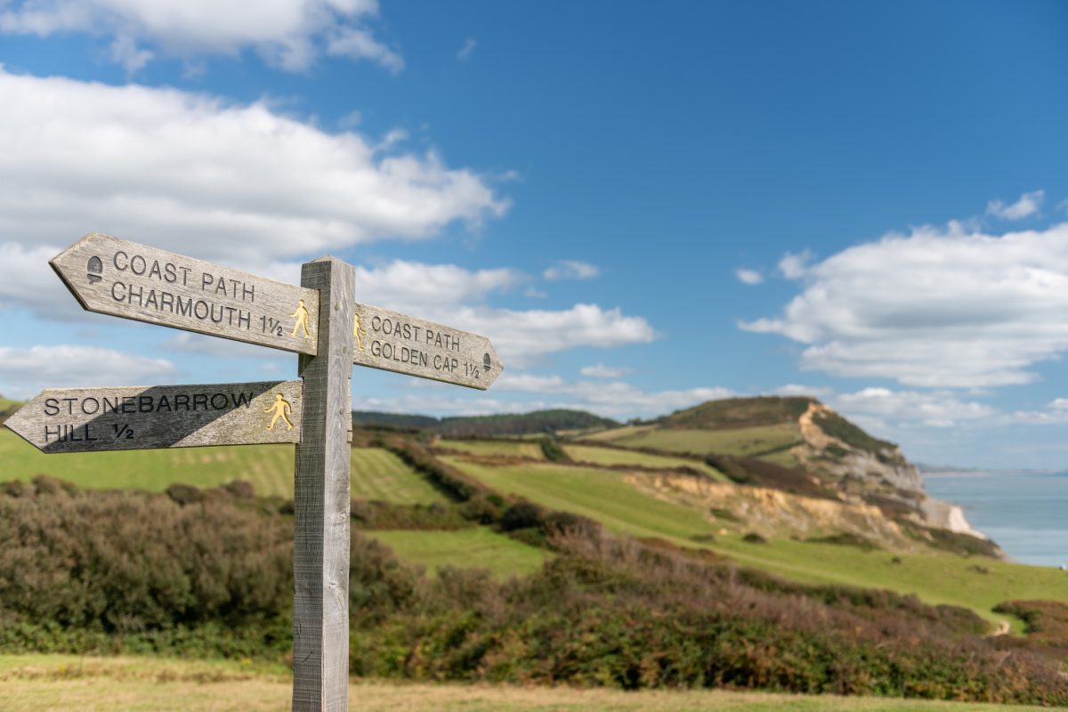 Coast path sign pointing towards Golden Cap with the landmark visible in the distance on the Dorset Jurassic Coast


