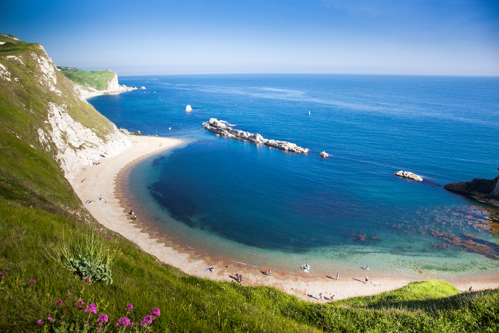 Hidden beach on the Jurassic Coast with blue sea, summer skies and wildflowers along the cliffs