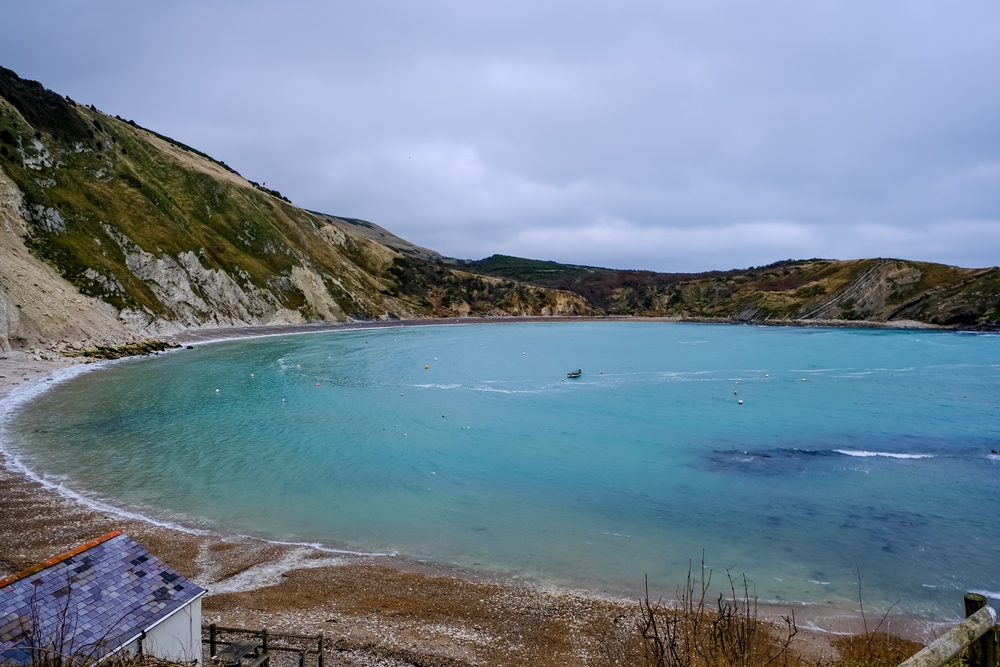 Lulworth Cove in Dorset with its blue sea beneath a cloudy sky