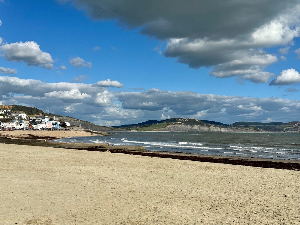 Lyme Regis beach and coastline beneath blue skies and dramatic clouds