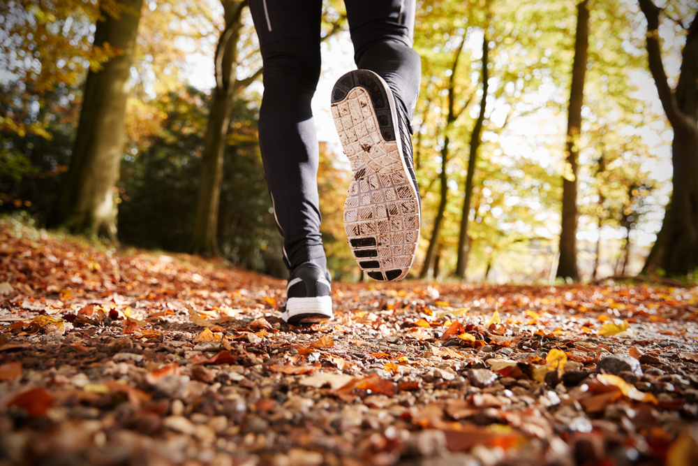 Runner on a woodland trail in autumn, with trainers and leggings visible among fallen leaves
