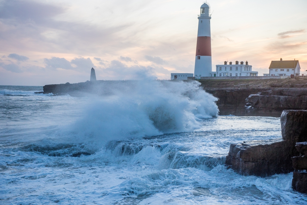 Waves crashing against the rocks with Portland Bill Lighthouse in the distance, Dorset.