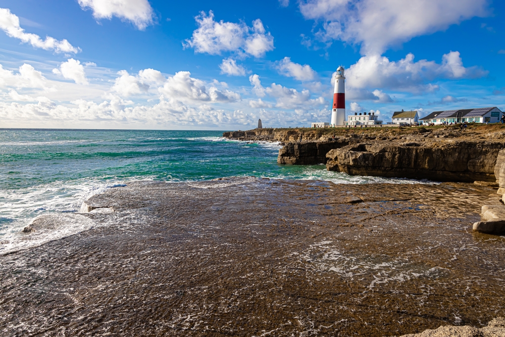 Portland Bill Lighthouse viewed across the rocky shoreline and clear blue sea in Dorset.