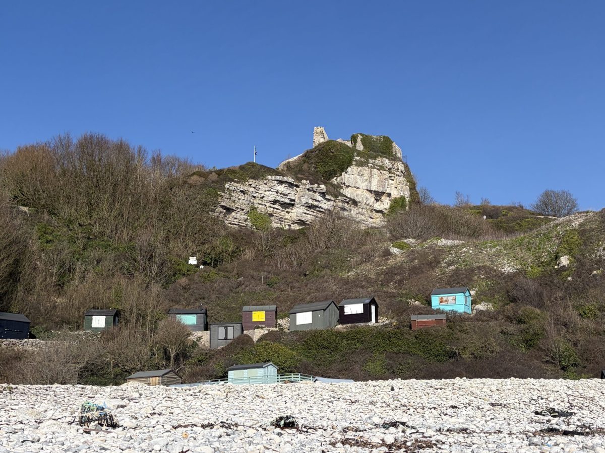 The ruins of Rufus Castle, beneath blue skies, overlooking the beach and beach huts at Church Ope Cove, Portland, Dorset.