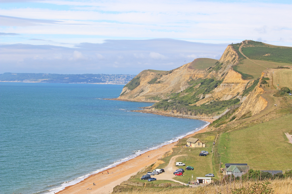 Clifftop view over Eype Beach on the Dorset Jurassic Coast with green cliffs beneath blue and grey skies