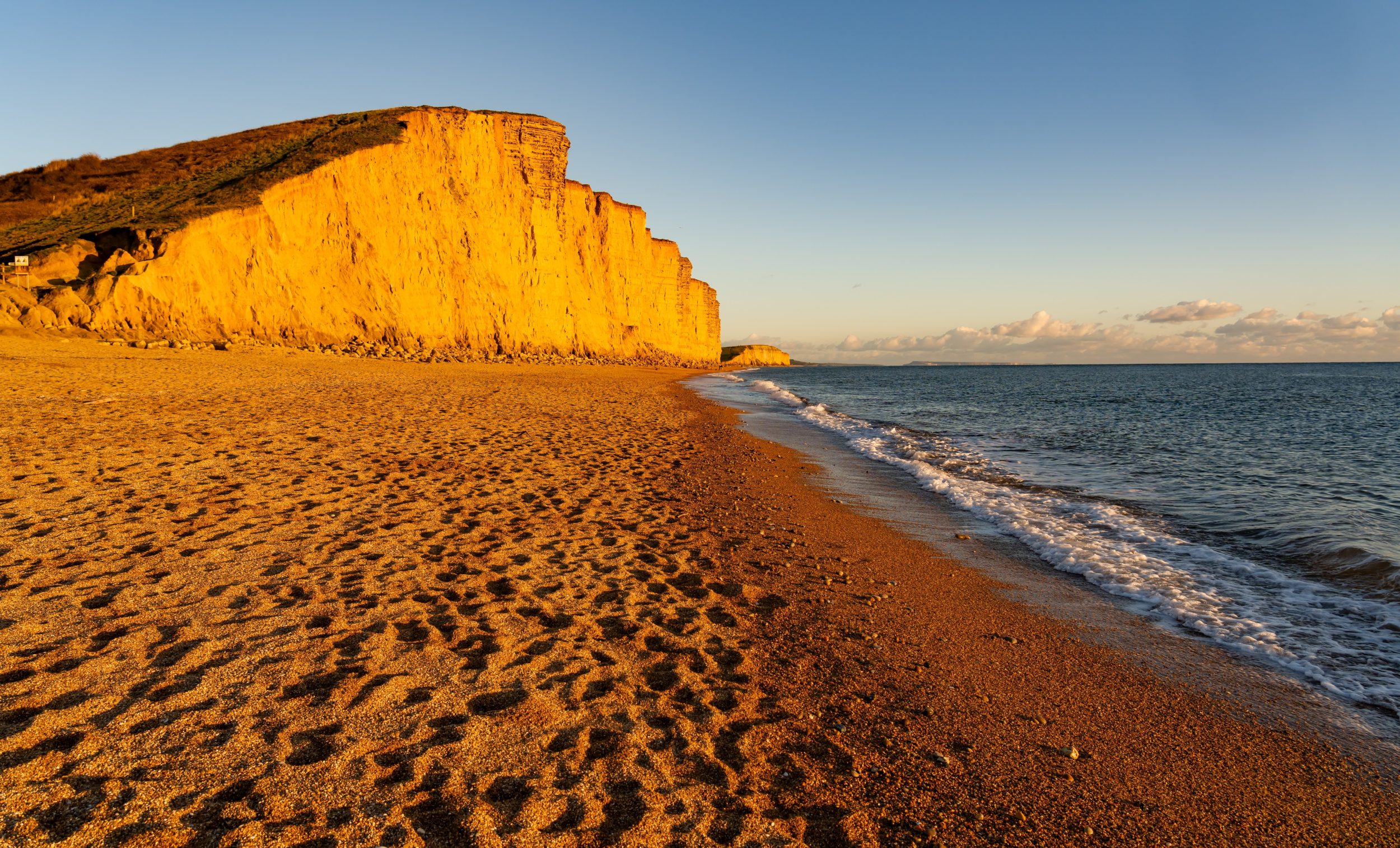 West Bay Beach glowing in the evening sun beneath the iconic golden cliffs on Dorset's Jurassic Coast.