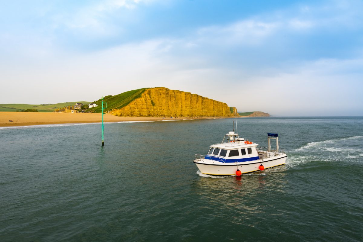 Fishing trip boat sailing past West Bay's golden cliffs on Dorset's Jurassic Coast.