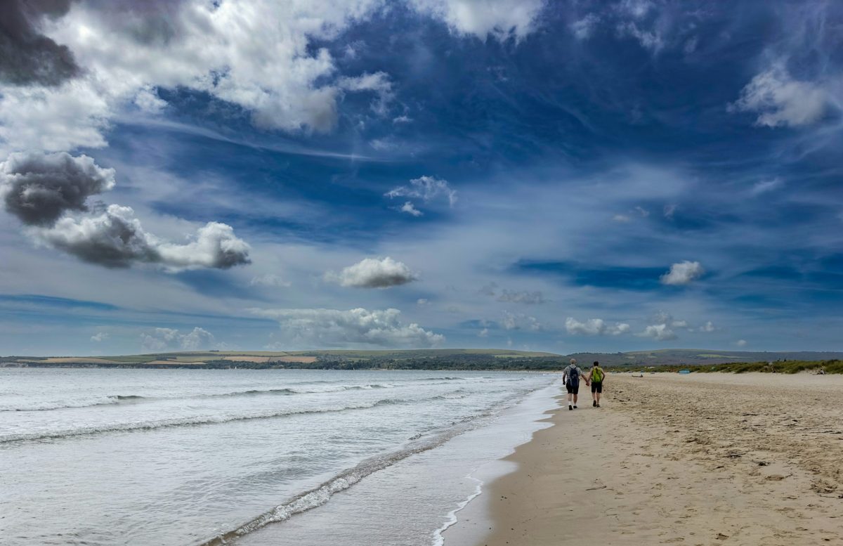 Couple walking along the shoreline at Knoll Beach in Studland, Dorset.