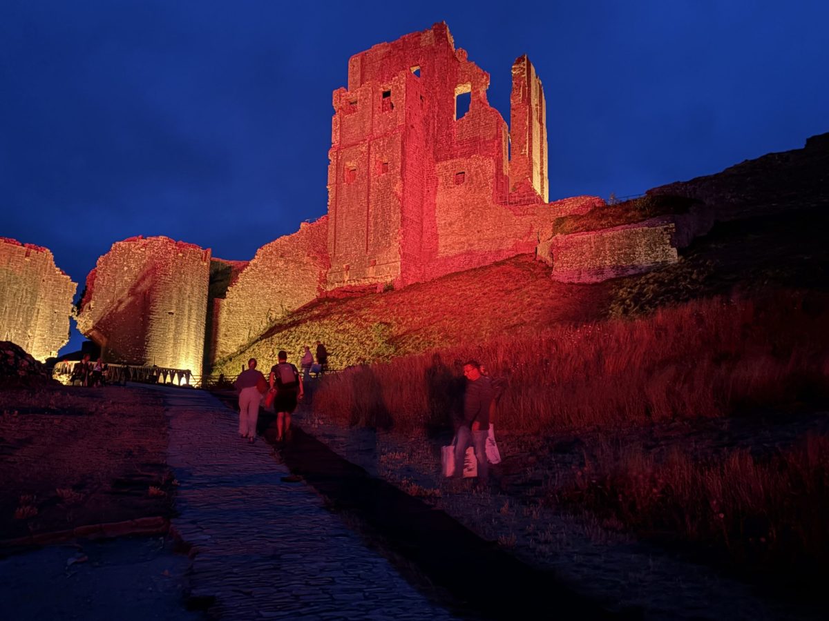 People walking up the illuminated path to Corfe Castle ruins at night
