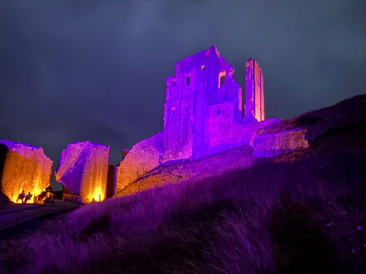 Corfe Castle ruins illuminated with purple lights at night
