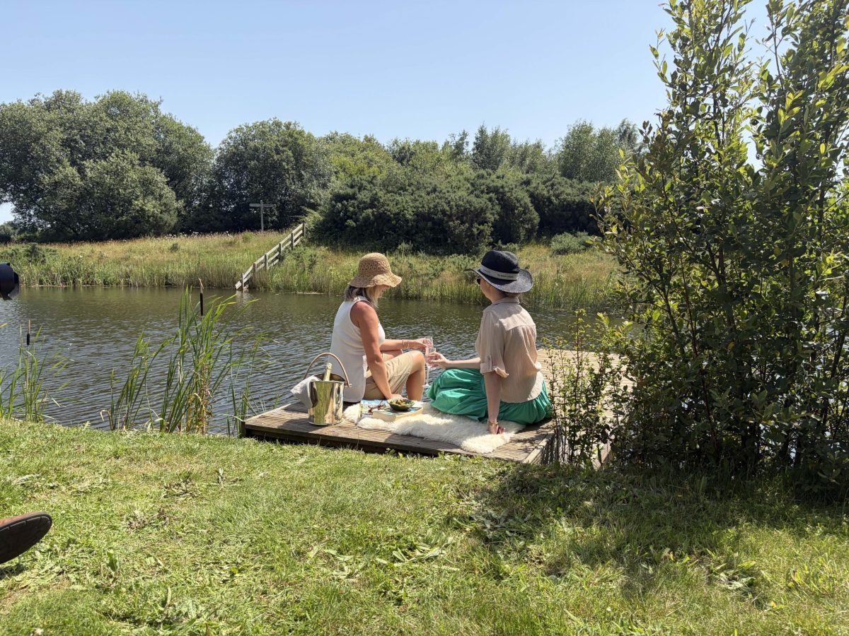 Two women enjoying champagne on a private lakeside jetty at a luxury holiday cottage on Silverlake Estate in Dorset.