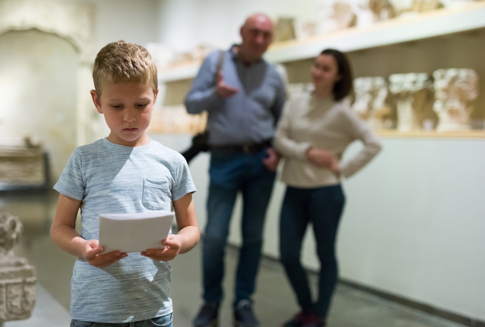 Young boy looking closely at a museum exhibit with his parents in the background.
