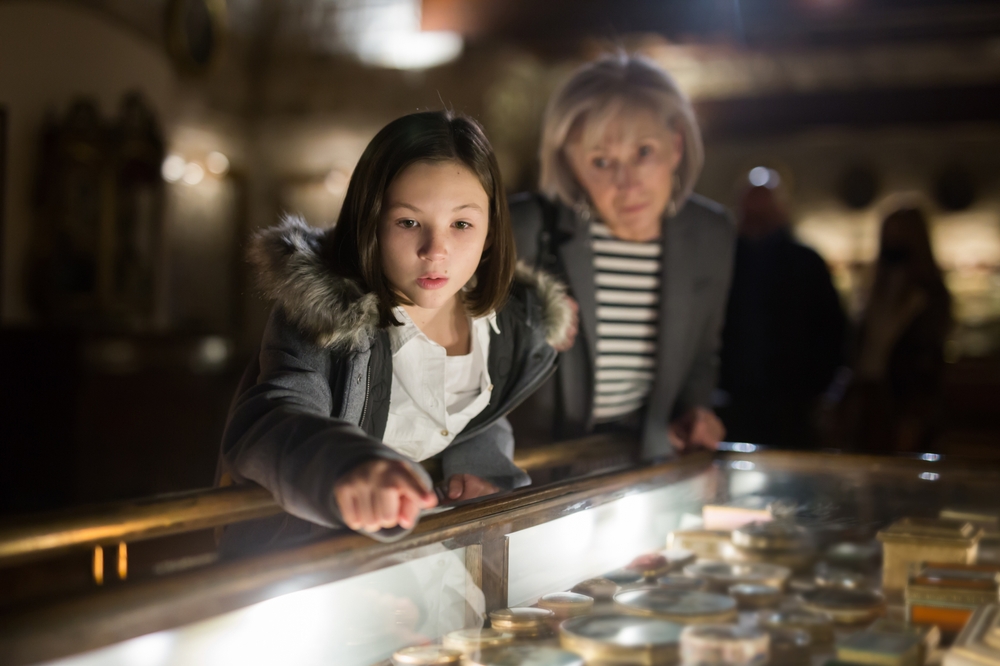 Young girl looking at a glass museum exhibit with her mother standing behind her.