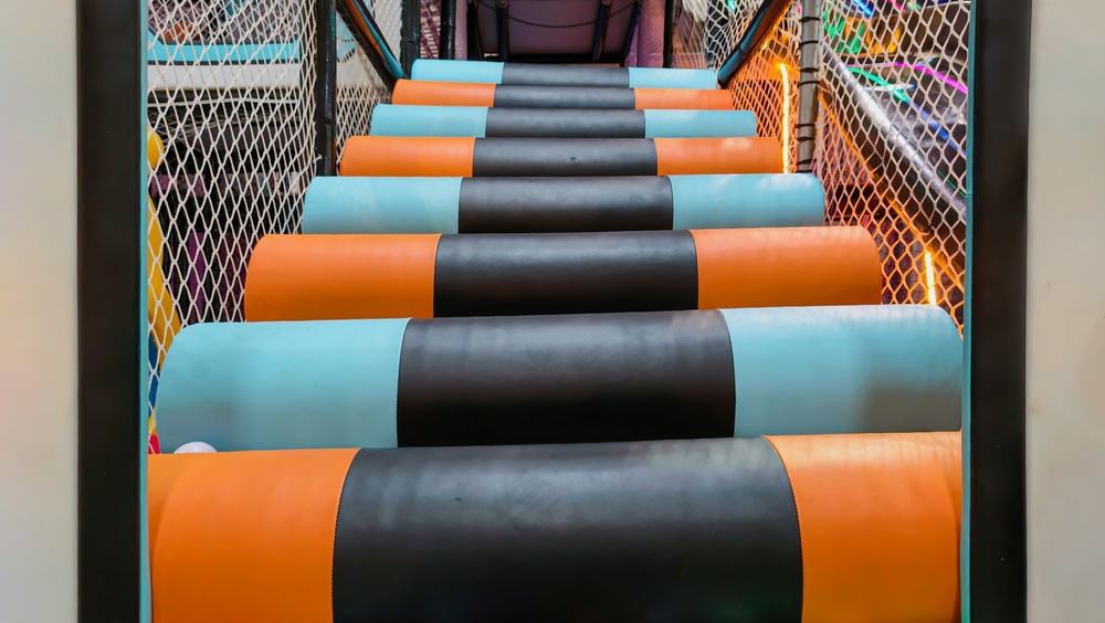 Colourful indoor soft-play area with padded steps and climbing equipment for young children.